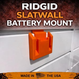 Puede incluir: Un soporte de bater&iacute;a Ridgid naranja para panel ranurado est&aacute; fijado a un panel ranurado blanco. El texto "RIDGID SLATWALL BATTERY MOUNT" est&aacute; en la parte superior de la imagen. La parte inferior de la imagen dice "MADE IN THE USA".