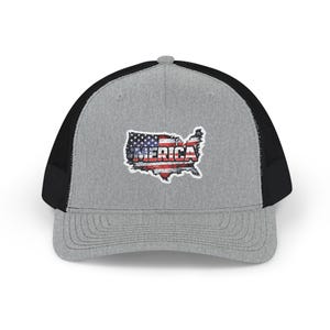 May include: A grey trucker cap with a black mesh back and a curved peak. The front displays a patch in the shape of the United States, with the word "AMERICA" in red and white, and a design resembling the American flag.