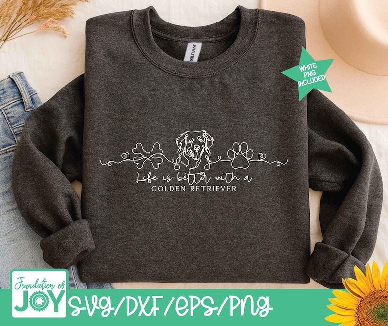 Op de afbeelding: Donkergrijze sweatshirt met de witte tekst "Life is better with a Golden Retriever". Het ontwerp bevat een bot, een hondenhoofd en een pootafdruk. De woorden "WHITE PNG INCLUDED" zijn ook zichtbaar.