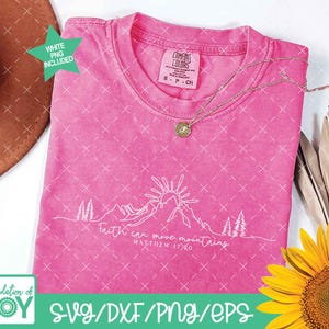 May include: A hot pink t-shirt with the text "Faith can move mountains" and a mountain graphic. The shirt has a crew neck and short sleeves. A gold necklace and a sunflower are also in the image.