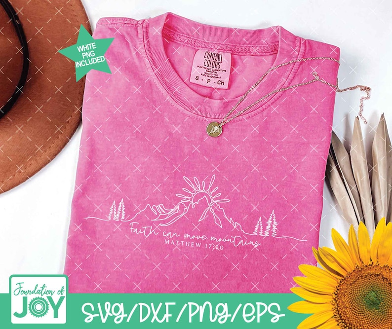 May include: A hot pink t-shirt with the text "Faith can move mountains" and a mountain graphic. The shirt has a crew neck and short sleeves. A gold necklace and a sunflower are also in the image.