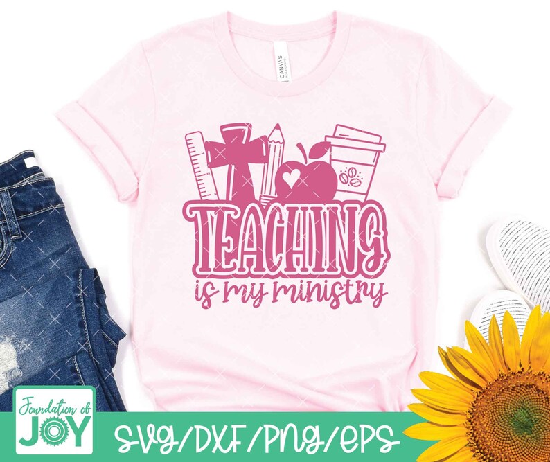May include: Pink t-shirt with a graphic design of a cross, a coffee cup, an apple, a ruler, and a pencil. The text "TEACHING is my ministry" is written in pink on the shirt.