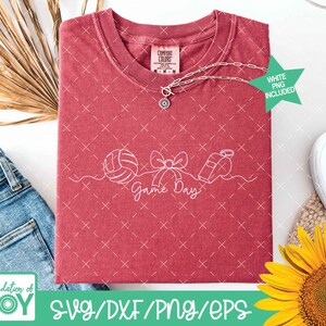 May include: A red t-shirt with a white graphic of a volleyball, bow, and whistle, with the words "Game Day." A silver necklace with a pendant is on the shirt. A green star indicates a white PNG is included.