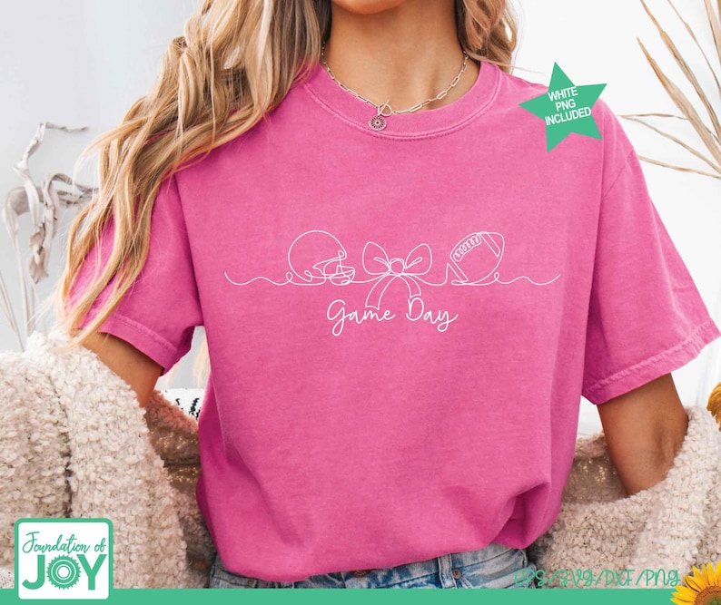 May include: A bright pink short-sleeve t-shirt featuring a white continuous line drawing of a football helmet, a bow, and a football. Below the graphic, the text Game Day is written in a white cursive font. A green star icon says WHITE PNG INCLUDED.