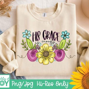 May include: A cream-coloured sweatshirt featuring the phrase "HIS GRACE is enough" in black script, decorated with watercolour-style flowers in yellow, purple, and blue. The sweatshirt has long sleeves and a crew neck. The image also includes the text "Png/Jpg Hi-Res Only".