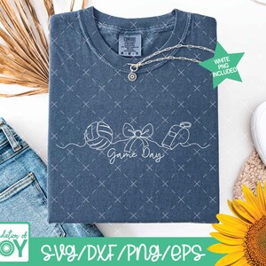 May include: A blue t-shirt with a white graphic of a volleyball, bow, and whistle, with the words "Game Day". The shirt has a crew neck and short sleeves. A silver necklace is draped on the shirt. The text "WHITE PNG INCLUDED" is on a green star.