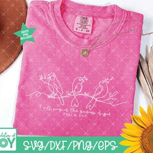 May include: A pink Comfort Colors t-shirt with a white line drawing of three birds on a branch. The text "I will sing of the goodness of God, Psalm 89:1" is below the birds. A gold necklace and a sunflower are also visible.