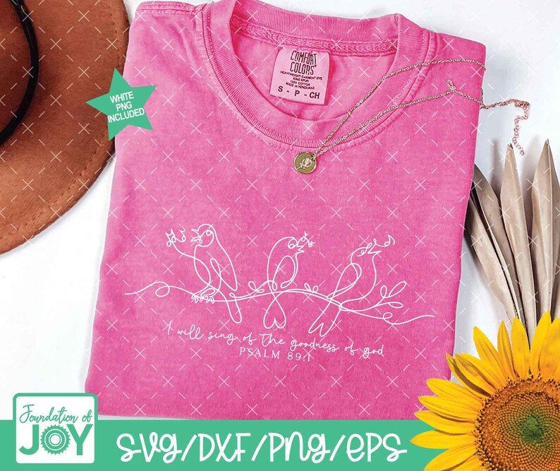 May include: A pink Comfort Colors t-shirt with a white line drawing of three birds on a branch. The text "I will sing of the goodness of God, Psalm 89:1" is below the birds. A gold necklace and a sunflower are also visible.