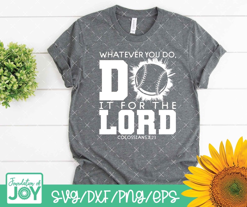 May include: A gray t-shirt with the text "WHATEVER YOU DO, DO IT FOR THE LORD COLOSSIANS 3:23" in white. A baseball graphic is centered above the text. The shirt has rolled-up sleeves and is displayed with a sunflower and greenery.
