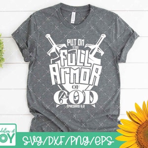 May include: A gray t-shirt with a white graphic design that says "Put on the Full Armor of God Ephesians 6:11". The graphic features two swords crossed over a shield.