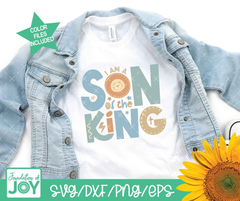 May include: A white t-shirt with the text "I am a Son of the King" in colorful letters with a lion graphic. The text is in a playful font with stars and a cross graphic. The t-shirt is displayed on a denim jacket and a sunflower.