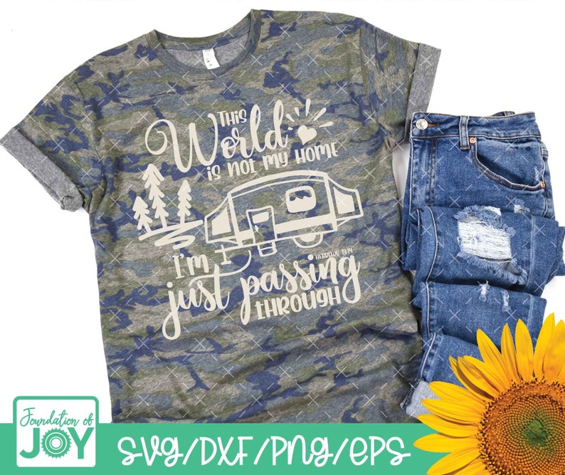 May include: A camouflage t-shirt with the text "This world is not my home I'm just passing through" and a small camper van graphic. The text is in a cream color. The t-shirt is on a white background with a pair of blue jeans and a sunflower.