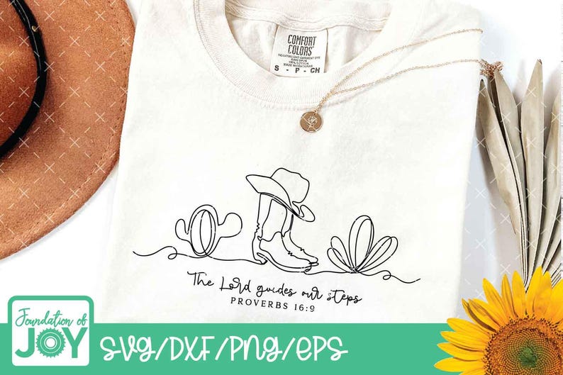 K&ouml;nnte beinhalten: Cremefarbenes T-Shirt mit einer schwarzen Strichzeichnung eines Cowboyhuts, Stiefel und Kakteen. Der Text "The Lord guides our steps" steht unter der Zeichnung. Eine goldene Halskette und ein brauner Hut sind ebenfalls zu sehen.