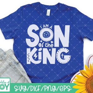 May include: A blue t-shirt with white text that reads "I am a Son of the King" with a crown and lightning bolt graphic. The shirt is on a white background with a pair of jeans and a sunflower.