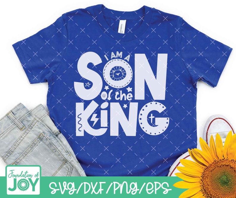 May include: A blue t-shirt with white text that reads "I am a Son of the King" with a crown and lightning bolt graphic. The shirt is on a white background with a pair of jeans and a sunflower.