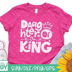 May include: Pink t-shirt with a white design that says "Daughter of the King" with a crown and a heart. The shirt has a white cross and a star.
