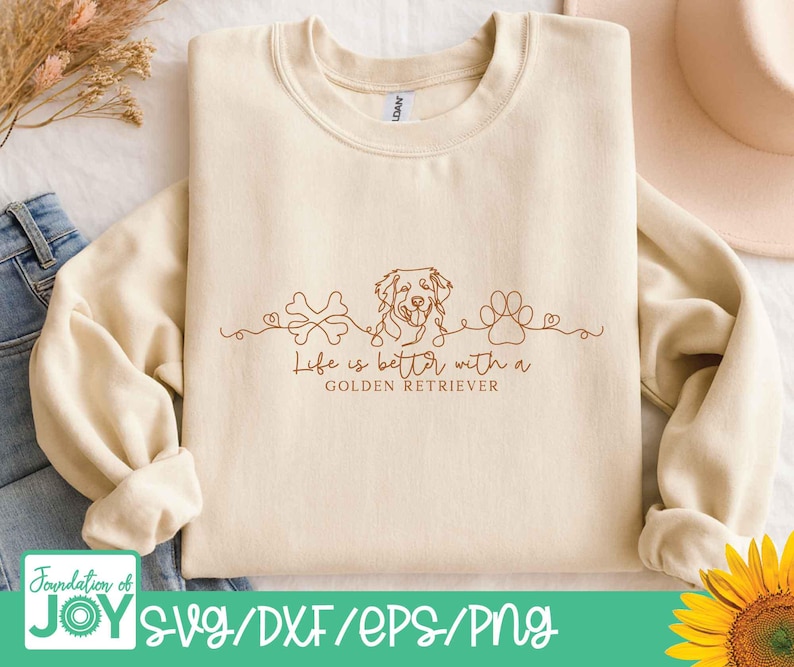 Op de afbeelding: Cr&egrave;mekleurige sweatshirt met een bruine lijntekening van een Golden Retriever, een bot en een pootafdruk. De tekst "Life is better with a Golden Retriever" staat onder de tekening. De onderkant van de afbeelding heeft de tekst "SVG/DXF/EPS/PNG".