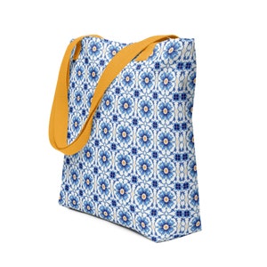 Op de afbeelding: Een witte tote bag met een blauw en geel bloemenpatroon. De tas heeft gele hengsels.