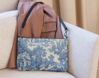 May include: A blue and white patterned clutch bag with a black strap. The bag is sitting on a light gray couch.