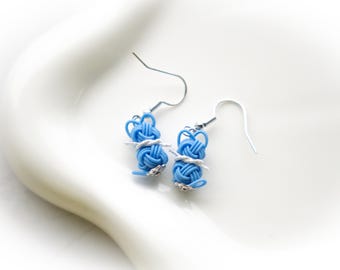 May include: A pair of blue and silver earrings with a knotted design. The earrings are made of a woven material and have a silver hook.