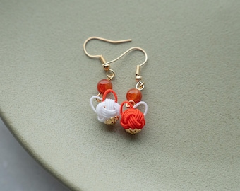 May include: A pair of earrings with red and white knotted balls and orange beads. The earrings are made with gold-colored metal.