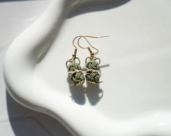 May include: A pair of green and gold earrings with a knotted design. The earrings are on a white surface.