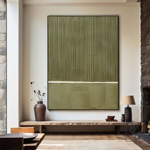Op de afbeelding: Abstract schilderij met verticale lijnen in tinten groen, gescheiden door een dunne witte lijn. Het schilderij is zwart ingelijst en hangt aan een witte muur boven een houten plank.