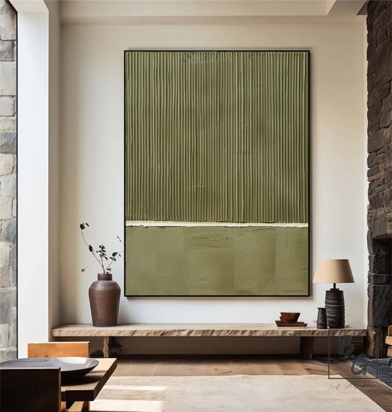 Op de afbeelding: Abstract schilderij met verticale lijnen in tinten groen, gescheiden door een dunne witte lijn. Het schilderij is zwart ingelijst en hangt aan een witte muur boven een houten plank.
