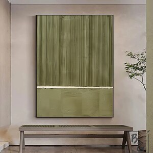 Op de afbeelding: Abstracte kunstprint met verticale lijnen in tinten van groen, gescheiden door een dunne witte lijn. De print is ingelijst in zwart en wordt weergegeven op een muur boven een houten bank.
