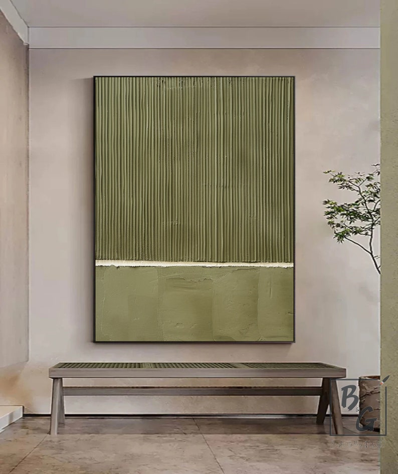 Op de afbeelding: Abstracte kunstprint met verticale lijnen in tinten van groen, gescheiden door een dunne witte lijn. De print is ingelijst in zwart en wordt weergegeven op een muur boven een houten bank.