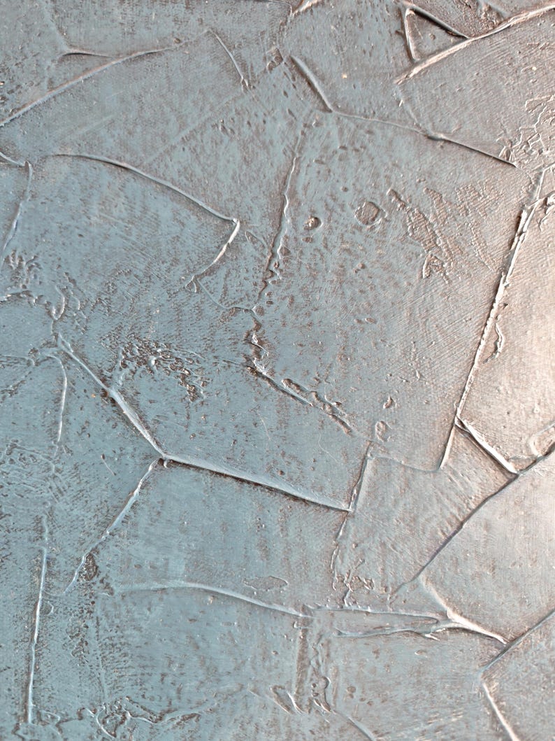 May include: Abstract textured artwork with a palette of muted blue and gray tones. The surface is composed of overlapping, irregular shapes, creating a layered effect. The texture appears rough and uneven, with visible brushstrokes and a subtle sheen.