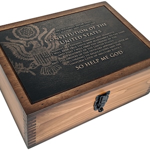 May include: A wooden box with a hinged lid and a metal latch. The lid features a black leather-like surface with an embossed image of the American eagle and the text "I do solemnly swear that I will support and defend the Constitution of the United States against all enemies, foreign and domestic; and that I will bear true faith and allegiance to the same; that I will obey the orders of the President of the United States and the orders of the officers appointed over me, according to regulations and the Uniform Code of Military Justice. So help me God."