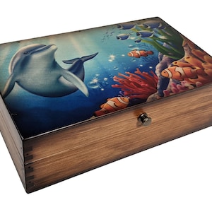 May include: A wooden box with a hinged lid featuring a colorful underwater scene with a dolphin, coral, and fish. The box has a brass latch.