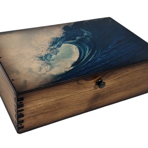 May include: A wooden box with a dark brown stain and a blue wave design on the lid. The box has a metal latch.