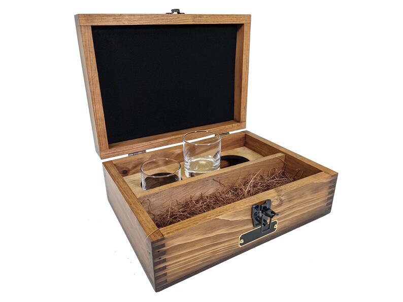 Puede incluir: Una caja de madera con tapa abatible, forrada de fieltro negro, y que contiene dos vasos de chupito de vidrio transparente. La caja tiene un cierre de lat&oacute;n y una peque&ntilde;a placa de nombre de lat&oacute;n.