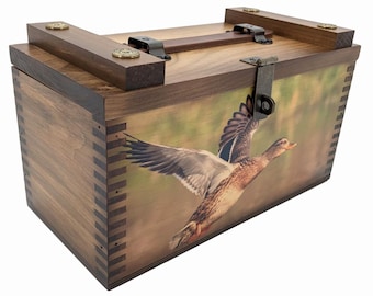 May include: A rectangular wooden box with finger-jointed corners, featuring a dark wood grain finish and a hinged lid. The front panel displays a printed image of a duck in flight. The lid includes a dark metal latch and a brown leather handle.