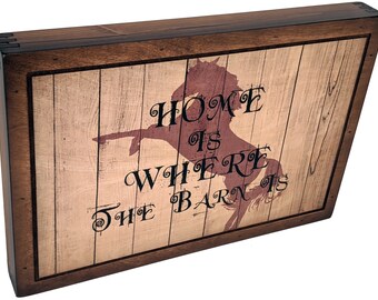 Könnte beinhalten: Ein Schild mit Holzrahmen und rustikalem Hintergrund, das eine Silhouette eines Pferdes mit dem Text "Home is where the barn is" zeigt.