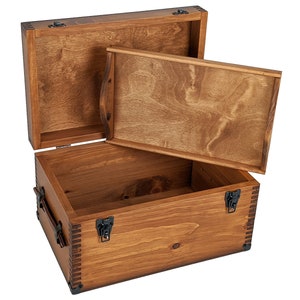 May include: A wooden storage chest with a hinged lid and a removable tray. The chest is made of natural wood with a light brown finish. The chest has black metal hinges and clasps.