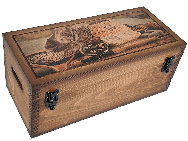 May include: A wooden box with a hinged lid and two clasps. The lid features a printed image of fishing gear, including a hat, fishing rod, reel, and tackle box.