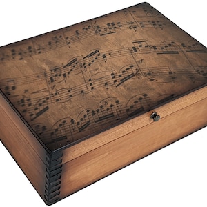 May include: A wooden box with a hinged lid. The lid is decorated with a printed design of musical notes. The box has a dark brown stain and a brass latch.