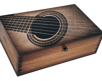 May include: A wooden box with a hinged lid and a metal latch. The lid features a laser-engraved image of an acoustic guitar with a soundhole and strings.