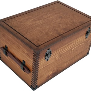 May include: A wooden storage chest with a hinged lid, brown leather handle, and metal accents. The chest is made of natural wood with a dark brown stain.