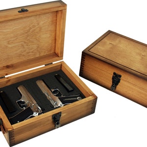 May include: A wooden box with a hinged lid, open to reveal two silver handguns and a magazine inside. The box has a brown stain finish and a metal latch.