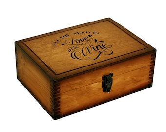 Puede incluir: Una caja de madera con tapa abatible y cierre. La tapa está grabada con el texto "Todo lo que necesitas es amor y vino".