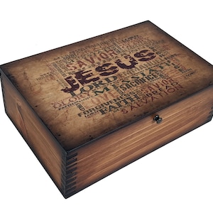 May include: A wooden box with a hinged lid and a metal latch. The top of the box is decorated with a vintage-style print of the word "Jesus" surrounded by other words related to faith and religion.
