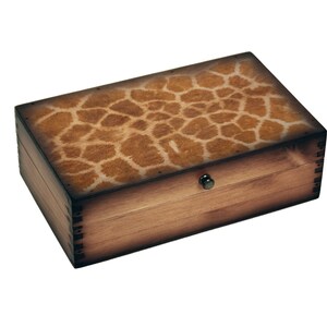 May include: Rectangular wooden box with a giraffe print lid. The box is made of light brown wood with darker edges and a small, round, black knob. The lid features a pattern of brown and tan spots.