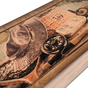 May include: A wooden box with a hinged lid. The lid features a printed image of fishing gear, including a hat, fishing rod, tackle box, and a fishing net. The background is a wood grain pattern.
