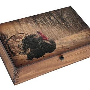 May include: A wooden box with a hinged lid and a metal latch. The lid features a printed image of a wild turkey in a snowy forest setting.