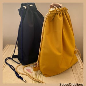 Peut inclure: Deux sacs à cordon, l'un bleu marine et l'autre jaune moutarde. Les deux sacs ont des cordons blancs et sont faits d'un matériau ressemblant à du canevas.