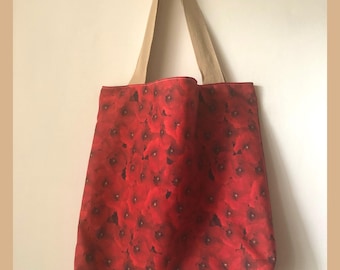 May include: A red tote bag with a floral print of red poppies. The bag has beige canvas straps.